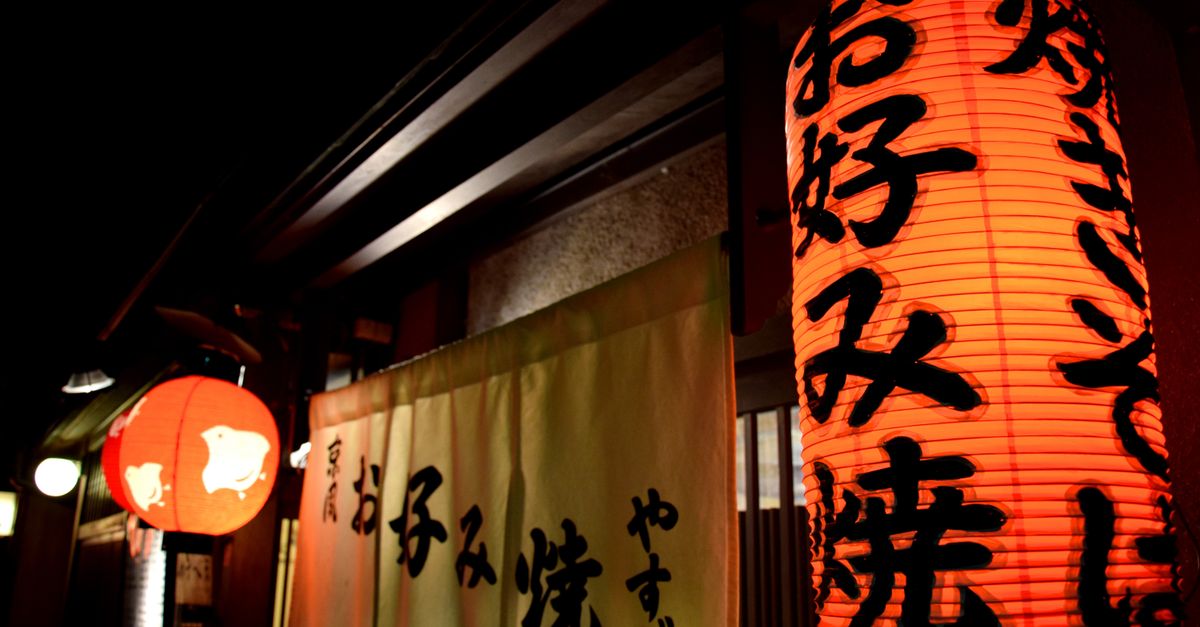 Illuminated Japanese lanterns with calligraphy hanging outside a building at night.